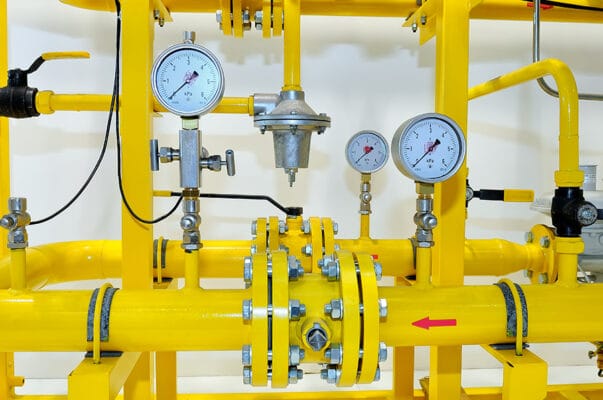 A group of yellow pipes and gauges in a room.