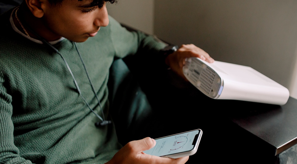 A man sitting on a couch with a cell phone, connected to IoT devices using Wi-Fi and Bluetooth modules.