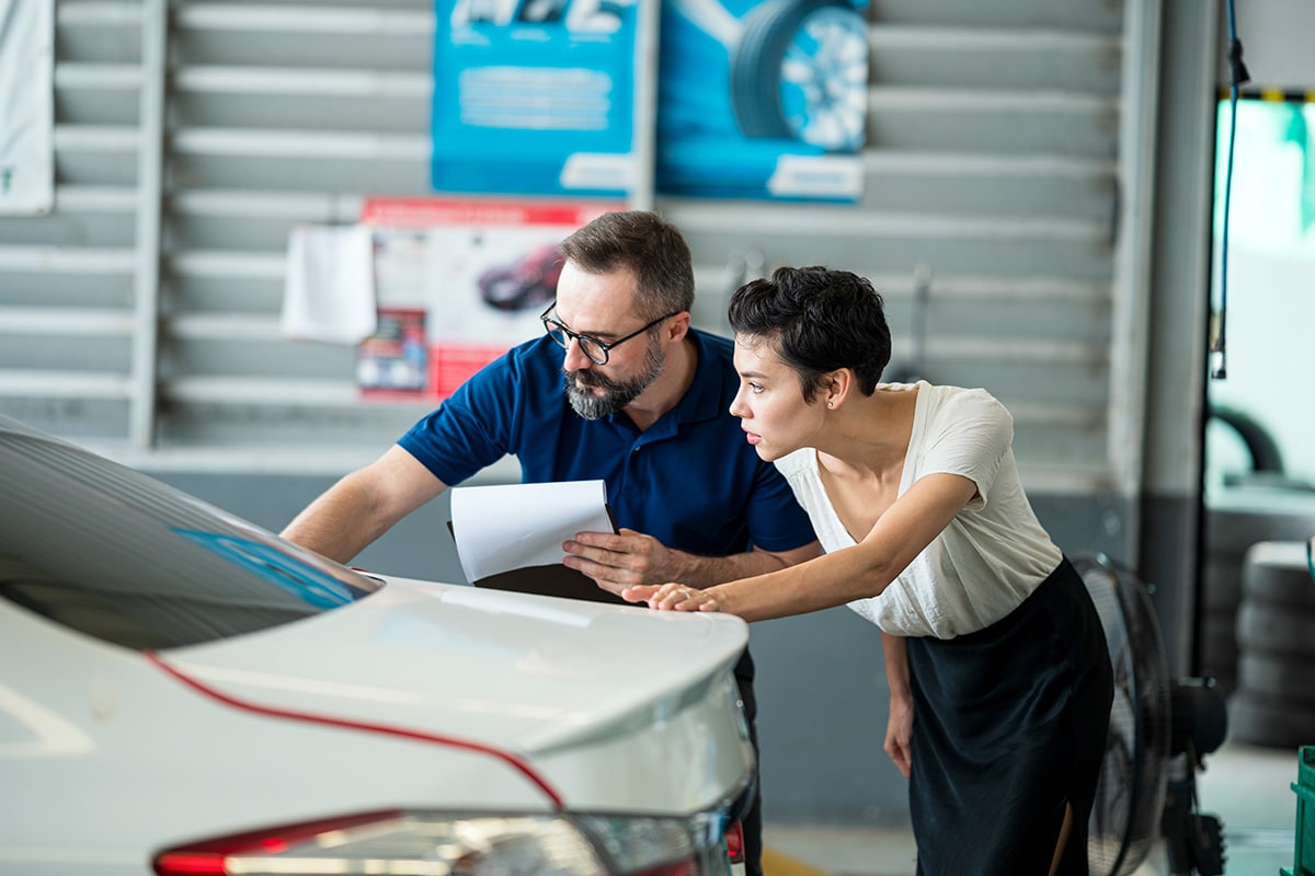 A man and woman examining a car in a garage for usage-based insurance.