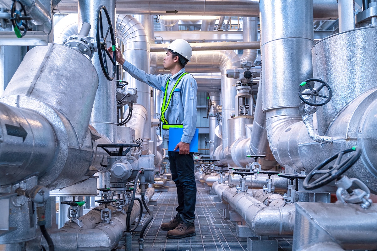 A man in a hard hat inspects pipes in a factory as part of smart waste and water management.