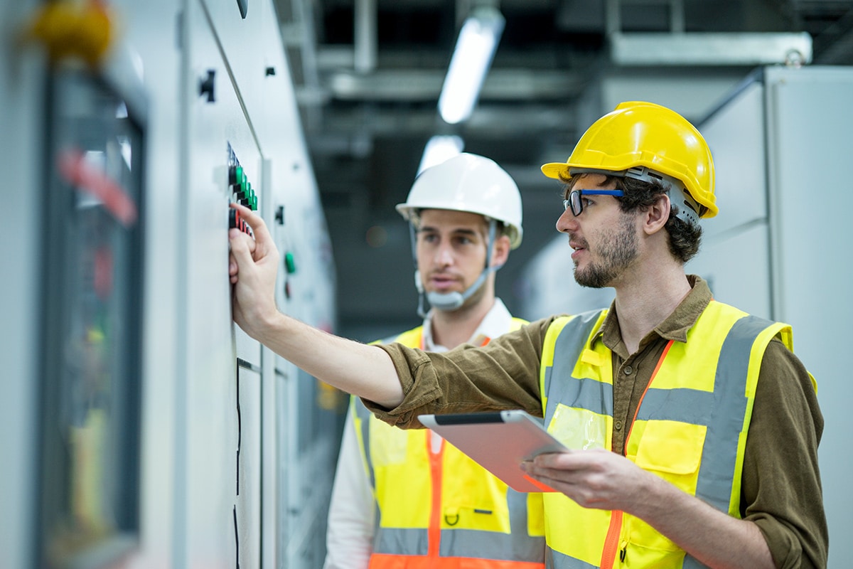 Two men in hard hats looking at an electrical panel.