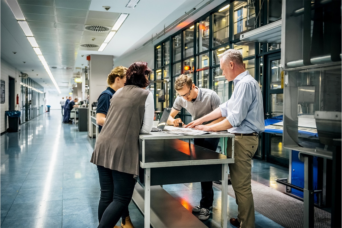 A group of people standing at a table in a long hallway, discussing Telit and Cinterion.