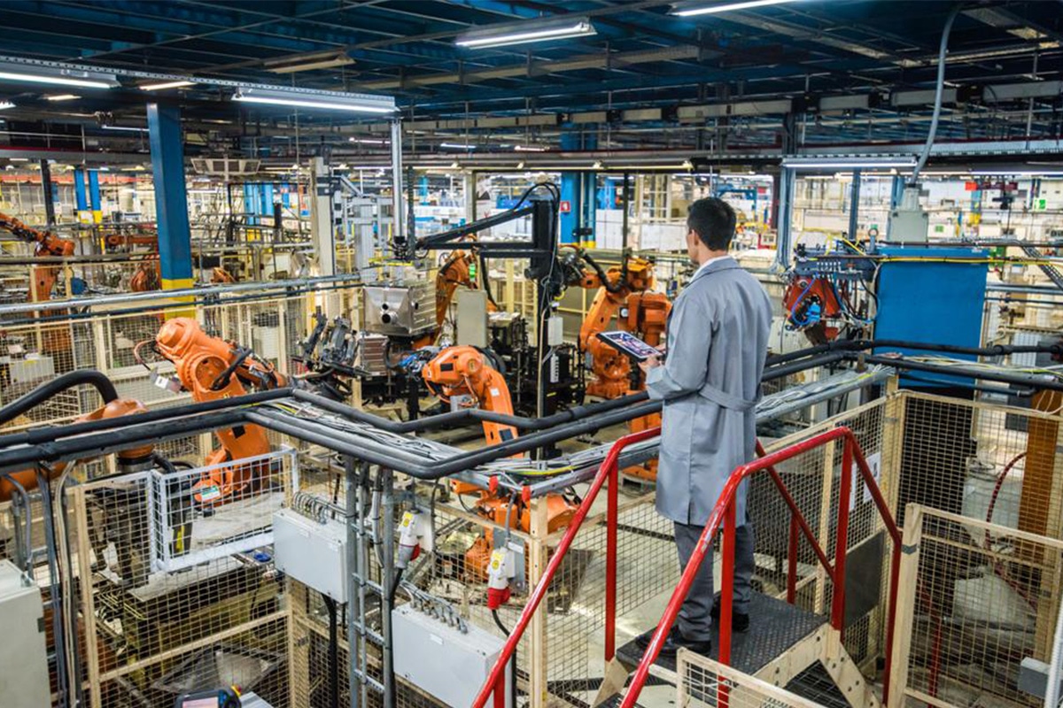 A man is standing on a ladder in a factory, overseeing the operation from above.