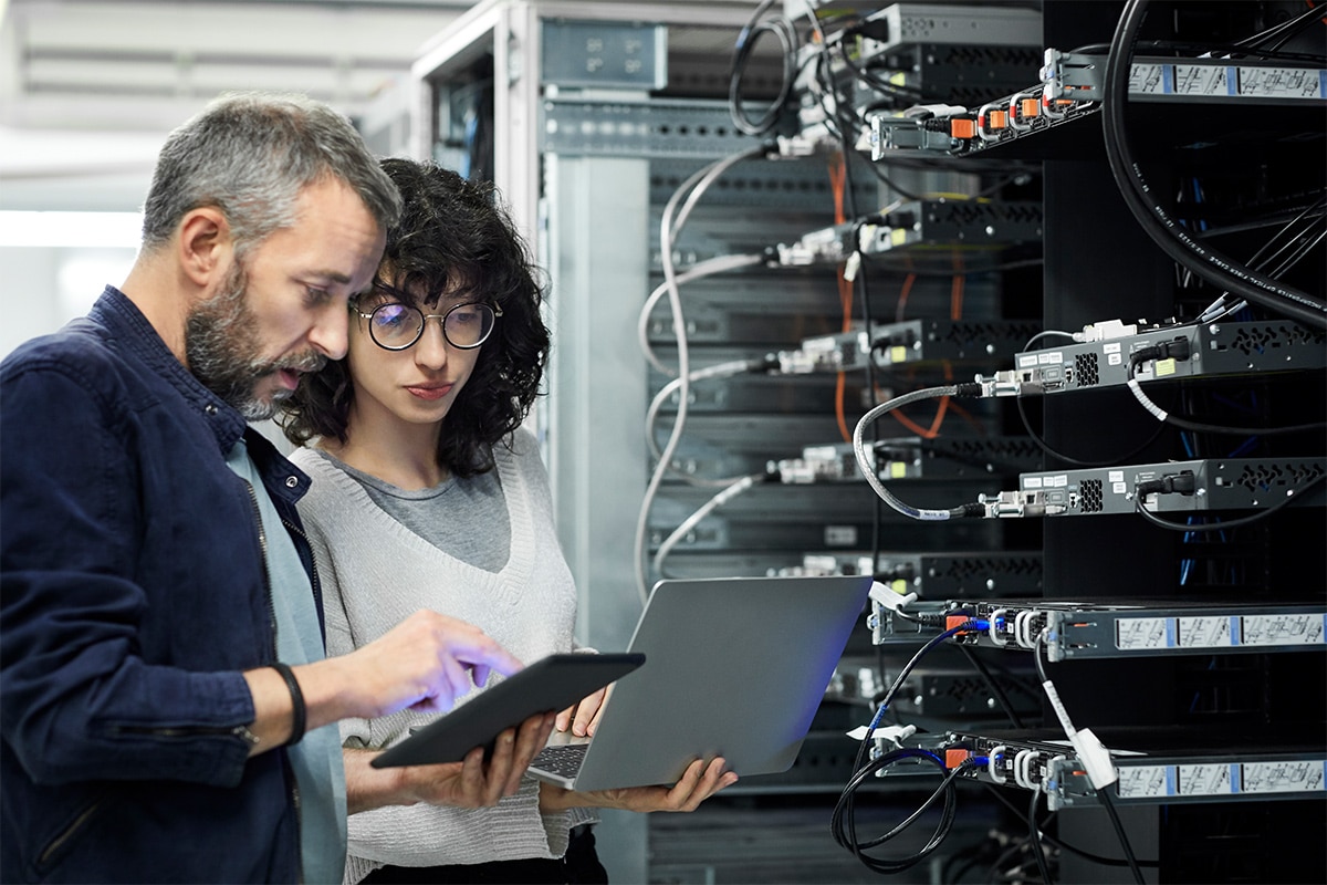 Two people looking at a laptop in a server room.