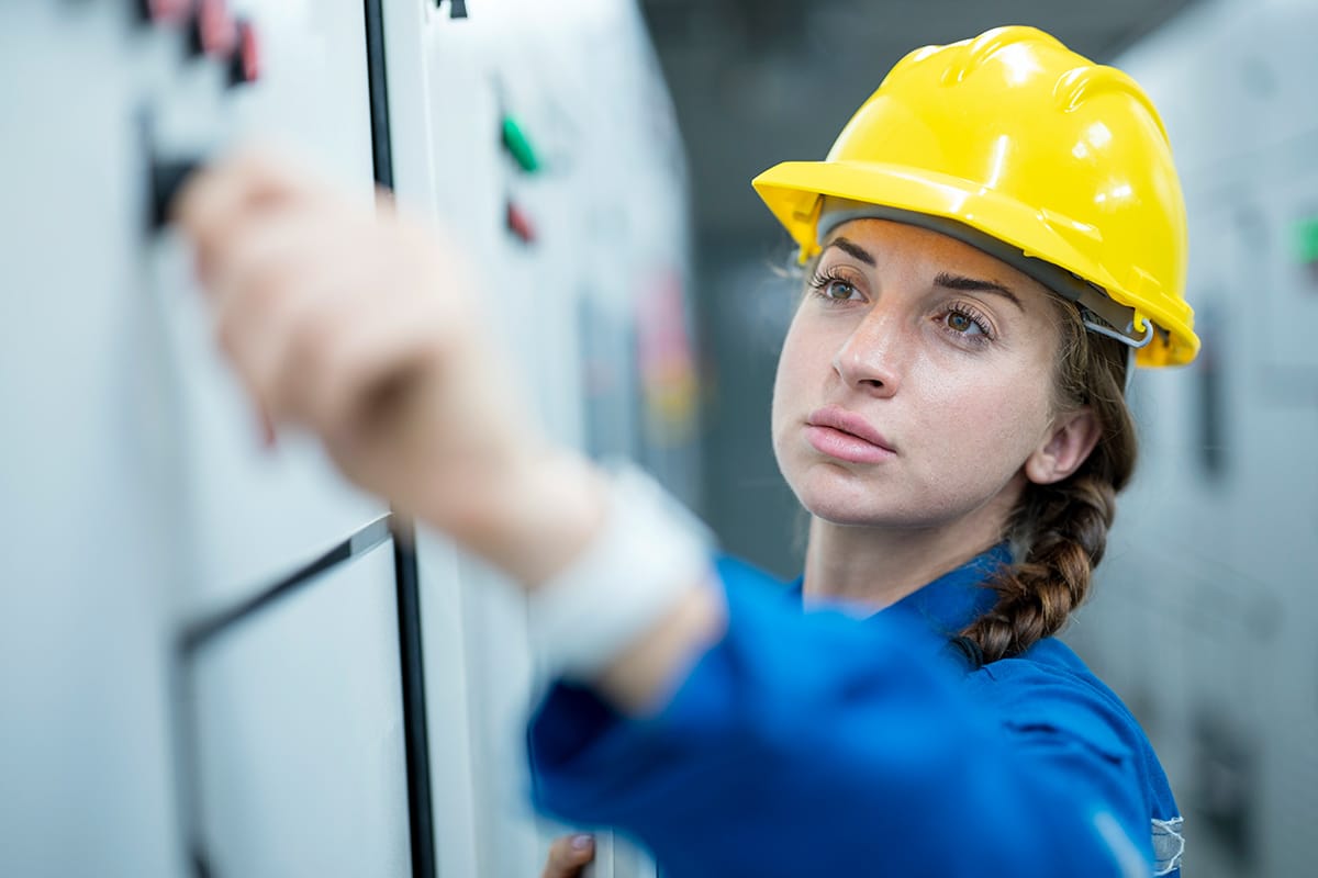 A woman in a hard hat is inspecting an electrical panel as part of a smart grid project.