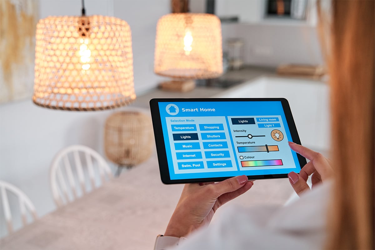 A woman is using an iPad to control her smart home with IoT solutions, including smart lighting.