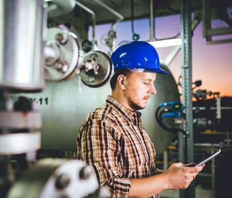 A man in a hard hat is using a tablet in a factory.