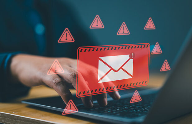 An envelope icon surrounded by red warning symbols overlays a person typing on a laptop.