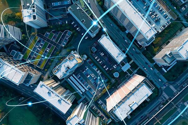 Aerial view of city buildings and roads with digital lines and glowing points illustrating data connectivity and urban technology.