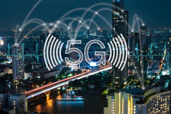The night cityscape dazzles as buildings and a bridge glow under digital graphics portraying 5G and IoT connectivity, illustrating a seamless fusion of technology with urban life.