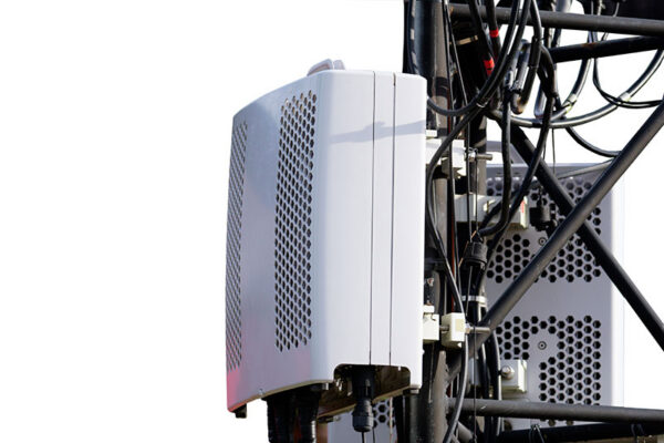 Close-up of a white 5G cellular small cell transceiver mounted on a metal tower structure with cables.