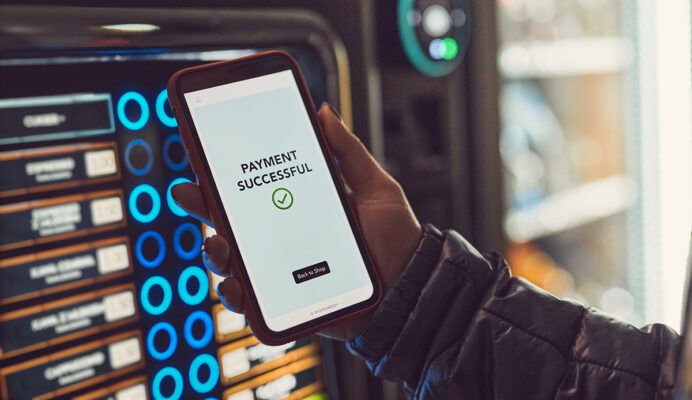 A person holding up a smartphone with a smart vending machine on it.