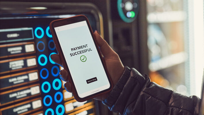 A person holding up a smartphone with a smart vending machine on it.
