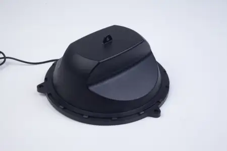 Black, dome-shaped electronic device with a cord attached, mounted on a circular base against a plain white background.