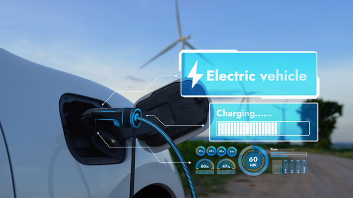 A white electric vehicle is charging at a station with a wind turbine in the background. A digital overlay displays charging progress and remaining time.