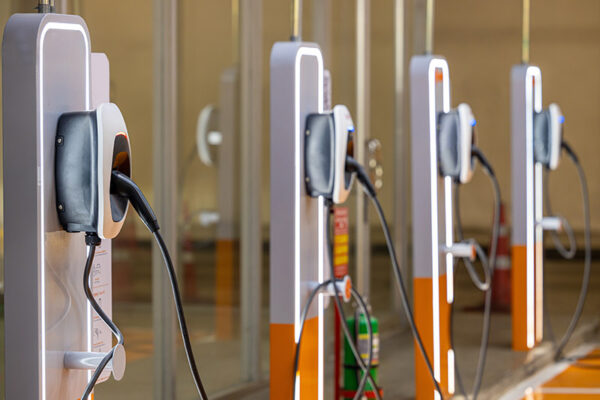 Several EV charging stations are lined up with charging cables plugged in.