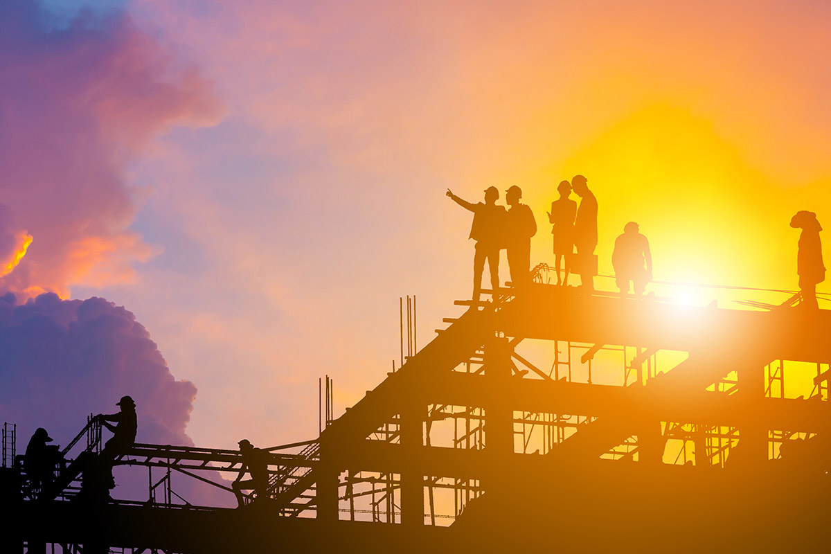 Silhouettes of construction workers on an IoT construction site at sunset.