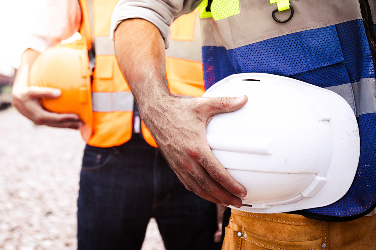 Two construction workers holding hard hats on a busy job site.