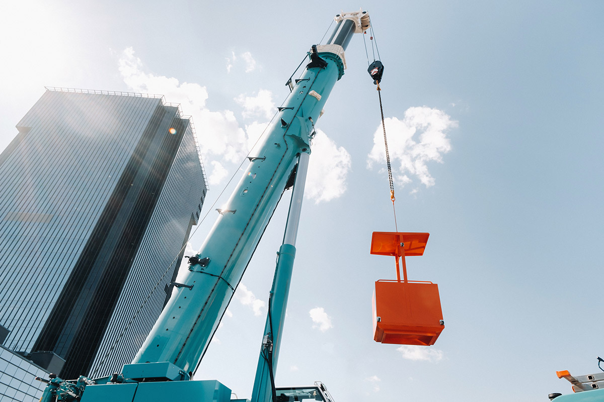 An IoT crane lifting an orange box in front of a skyscraper.