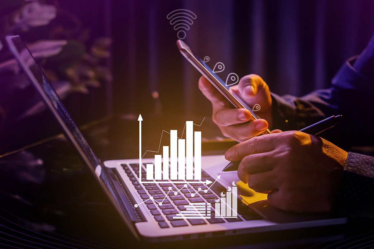 A person using a laptop with IoT data displayed on graphs.