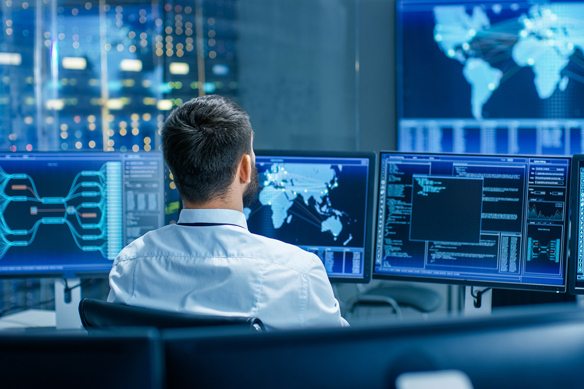 A man in a white shirt is monitoring multiple screens for engineering and R&D services.