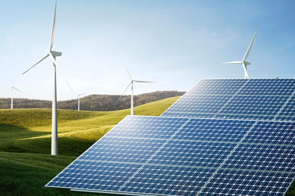 Solar panels and wind turbines stand in a grassy landscape under a clear sky.