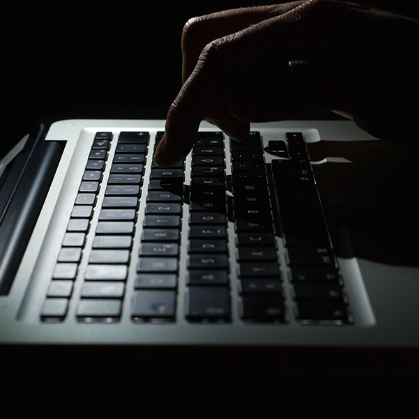 A shadowy figure typing on a laptop keyboard.