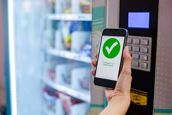 A person holding a smartphone up to a smart vending machine to pay for their items.