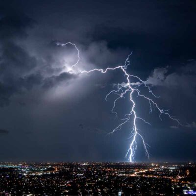 A bright bolt of lightning illuminating the night sky over a city.