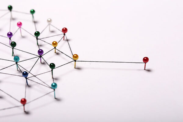Colored pins connected by black thread form a network on a white surface, visually representing mobile network operators, with one red pin isolated outside the main group.