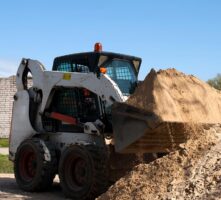 Compact tractor and loader hauling dirt.