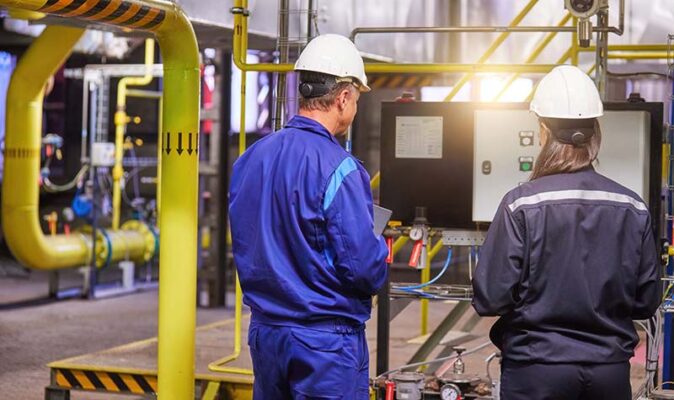 Two workers perform a maintenance check on machinery.