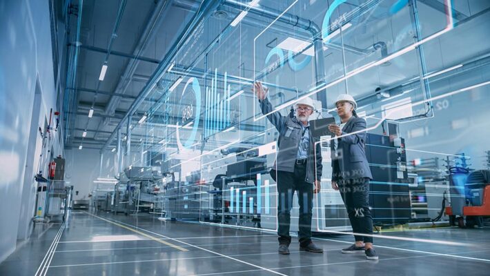 Factory digitalization: Two industrial engineers using a tablet computer and visualizing a wall of big data statistics.