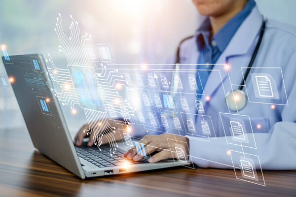 Digital medical records and data icons are superimposed over a person in a white coat using a laptop.