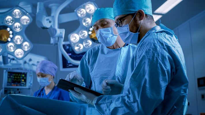 Two surgeons in an operating room using a tablet to utilize 5G technology in health care.
