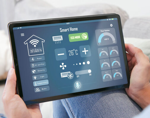 A person holding a tablet displaying a smart home control interface, with icons for temperature, lighting, security, smart meters and other functions.
