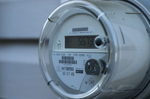A smart electric utility meter displaying readings, mounted on a wall with visible technical labels and specifications.
