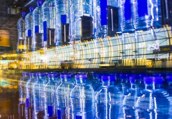 Blue water bottles displayed on a smart vending machine's reflective surface with blurred background.