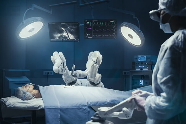 A patient lies on an operating table as robotic surgical arms perform a procedure. A medical professional monitors the procedure using electronic displays in the operating room.