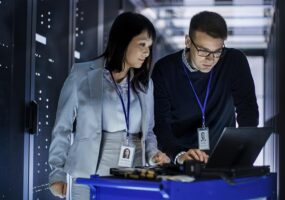 Two individuals collaborating on a laptop in a server room for IoT cloud integration.