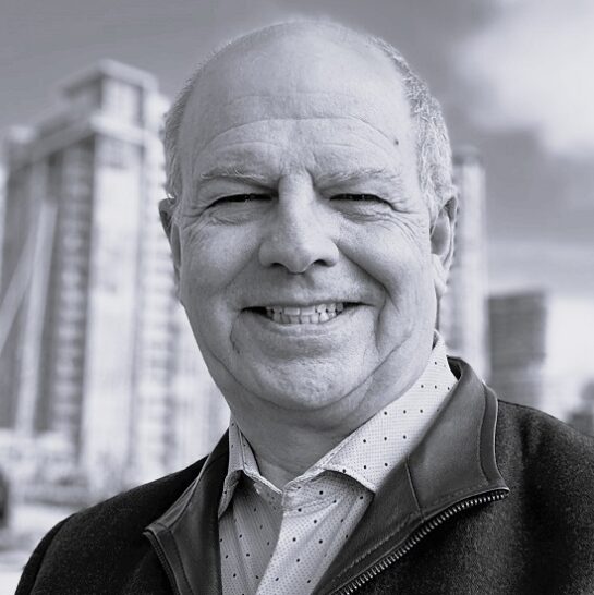 Black and white picture of Roy MacLean with buildings in the background.