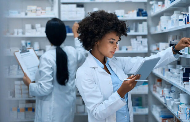Two pharmacists in lab coats work in a pharmacy.