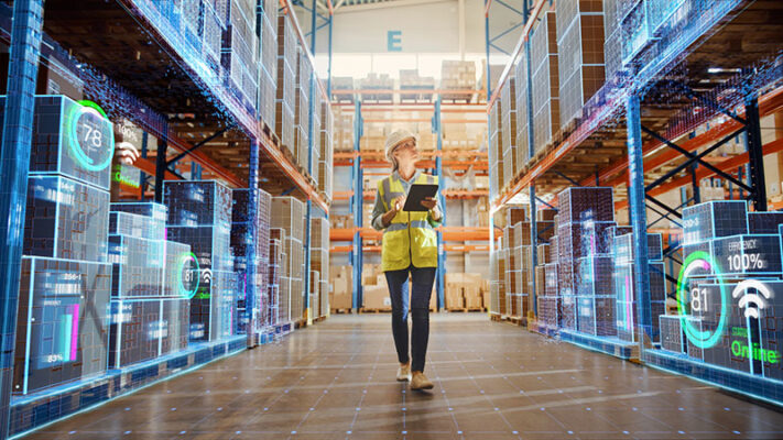 Worker inspecting inventory data on a tablet in an IoT-enabled supply chain warehouse.