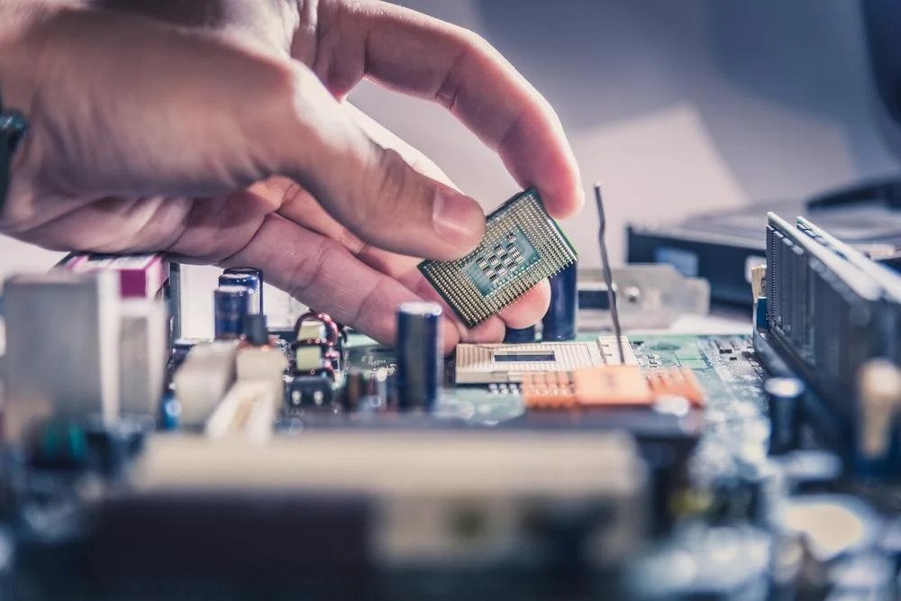 A person's hand installing a CPU on a motherboard, with other computer components and tools blurred in the background.