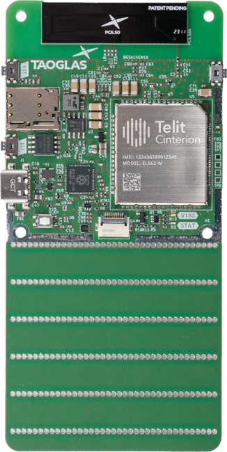 Close-up of a green electronic circuit board featuring various components including microchips, connectors, and antenna modules labeled "taoglas" and "telit.
