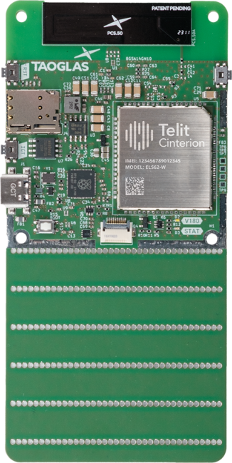 Close-up of a green electronic circuit board featuring various components including microchips, connectors, and antenna modules labeled "taoglas" and "telit.