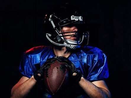 A football player holding a ball in a dark room.