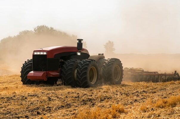 A red, self-driving tractor with large tires plowing a dry, dusty field, showcasing  precision agriculture.