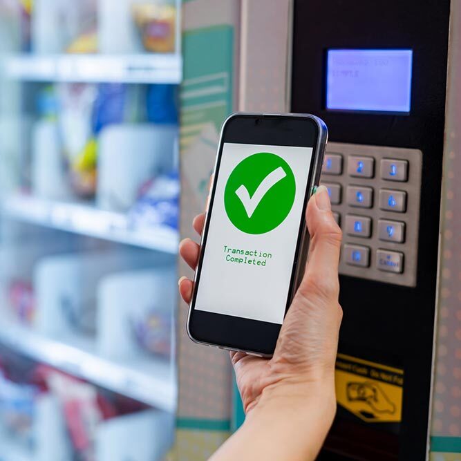 A person holding a smartphone up to a smart vending machine to pay for their items.