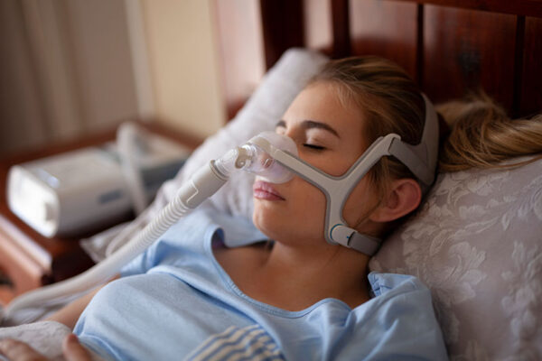 A person is comfortably sleeping in bed with a CPAP mask on, a testament to medtech advancements and the benefits of RTM device reimbursement.
